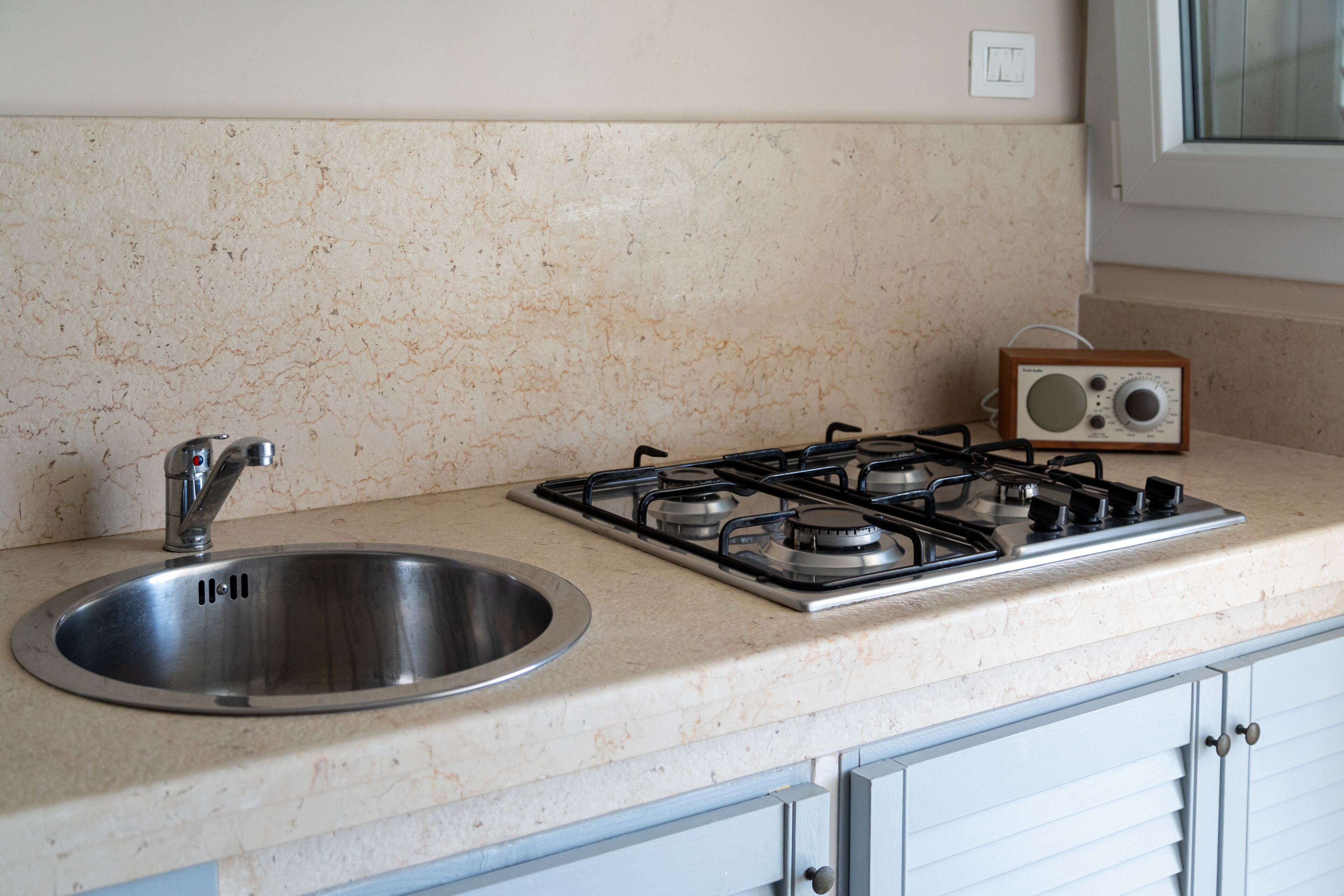 A kitchen with a stainless steel sink, a gas stove, and a wooden radio.