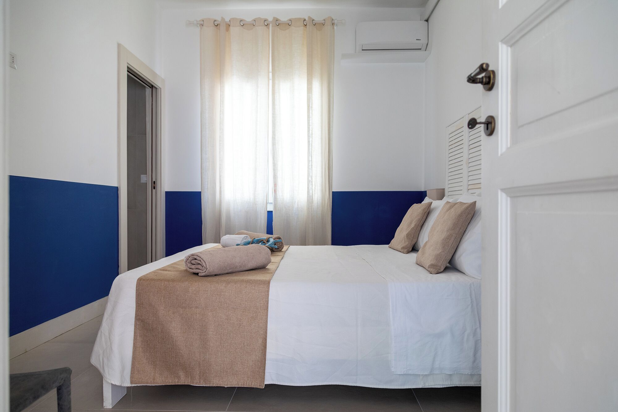 Une chambre à coucher avec un lit, une fenêtre avec des rideaux, une porte et un climatiseur fixé au mur.