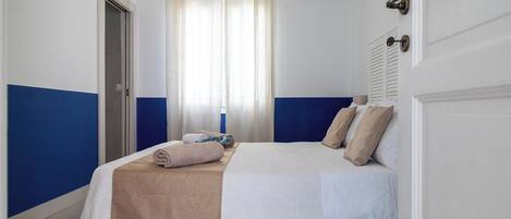 Une chambre à coucher avec un lit, une fenêtre avec des rideaux, une porte et un climatiseur fixé au mur.