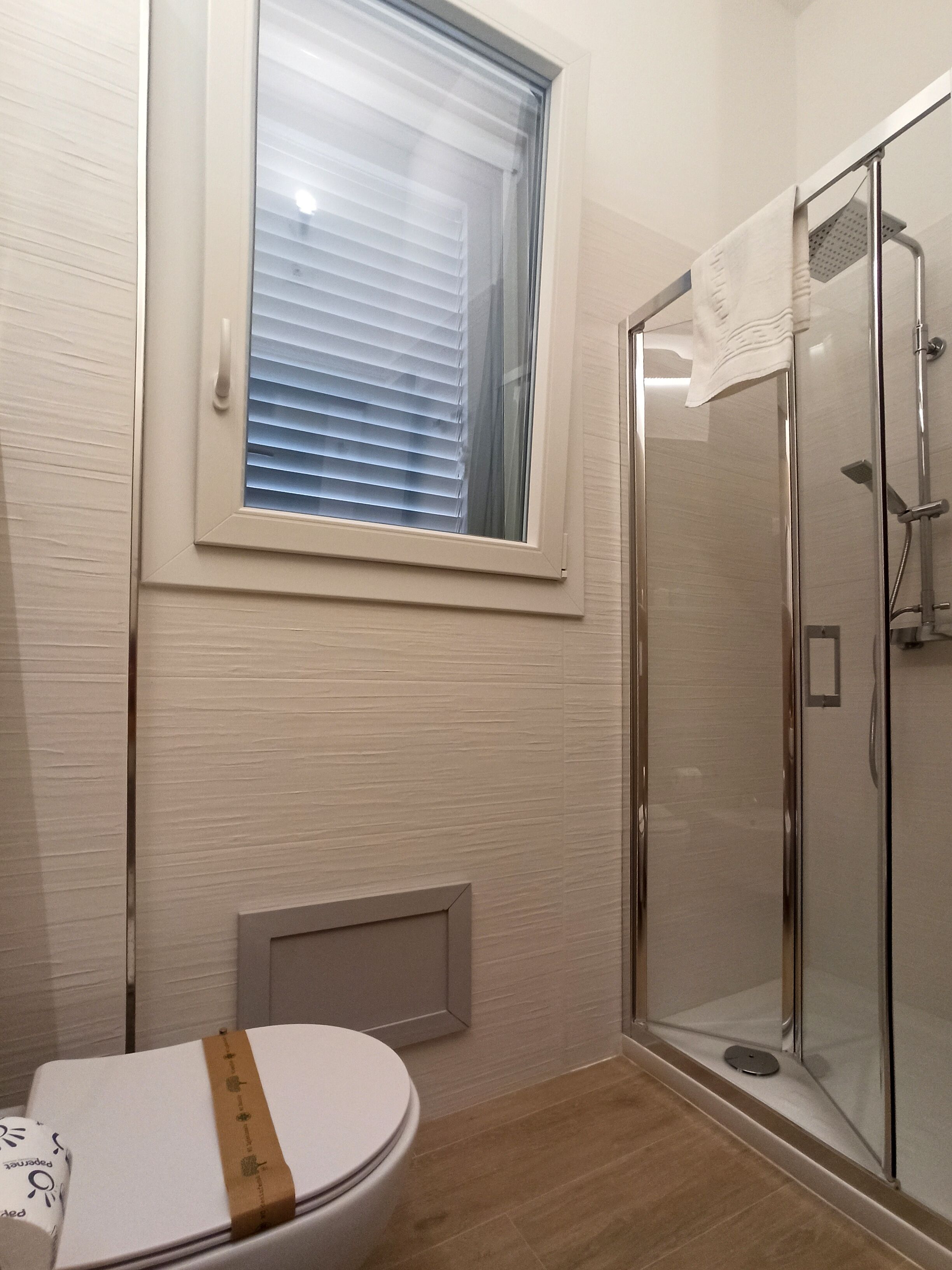 A bathroom with a toilet, a shower, and a window with blinds.