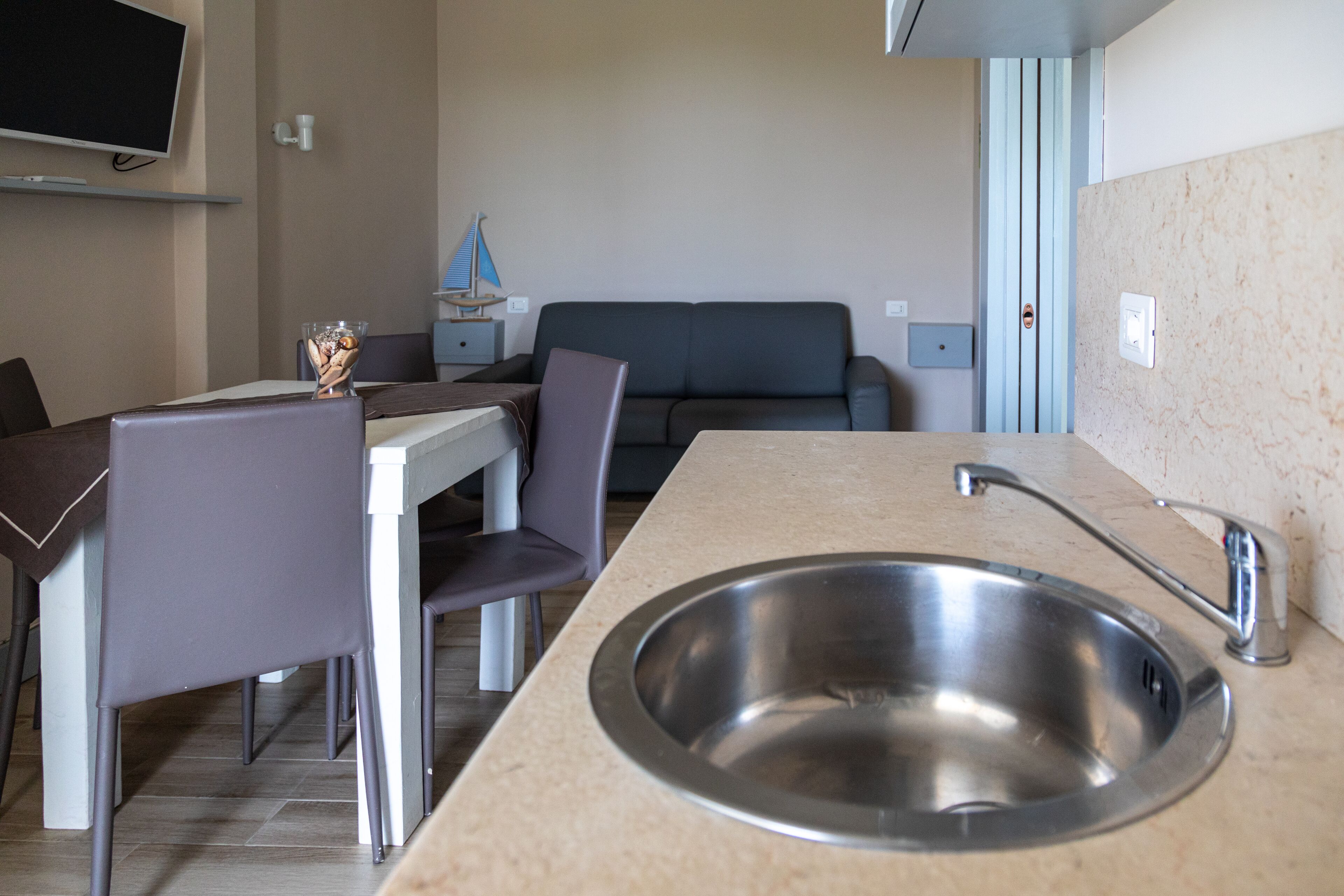 Une cuisine moderne avec un évier en acier inoxydable, une table à manger avec des chaises et un canapé à l’arrière-plan.