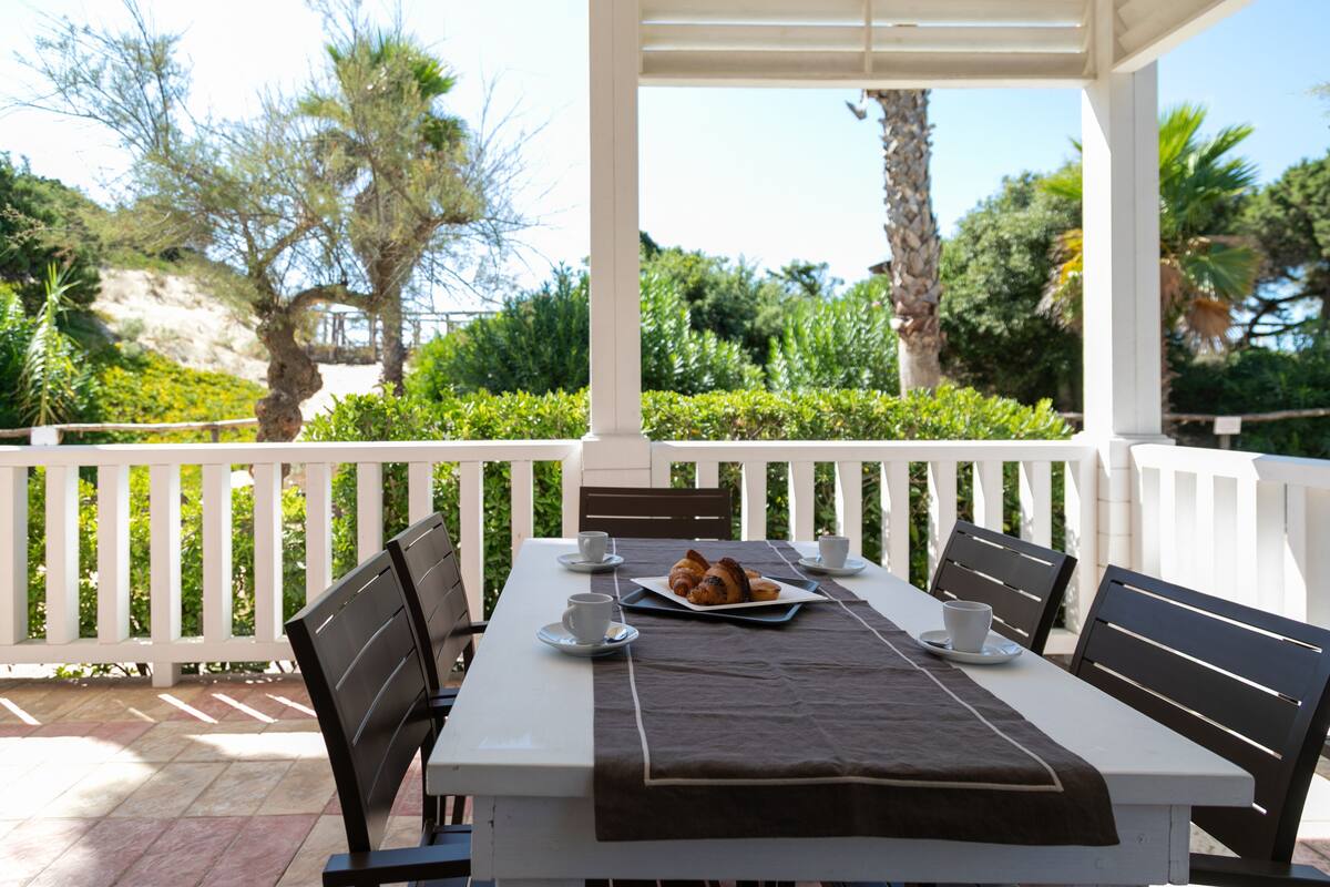 A covered outdoor dining area with a white table, black chairs, and a brown table runner.
