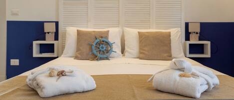 Habitación de hotel con cama, dos toallas blancas, una decoración con timón de barco y una pared azul de acento.