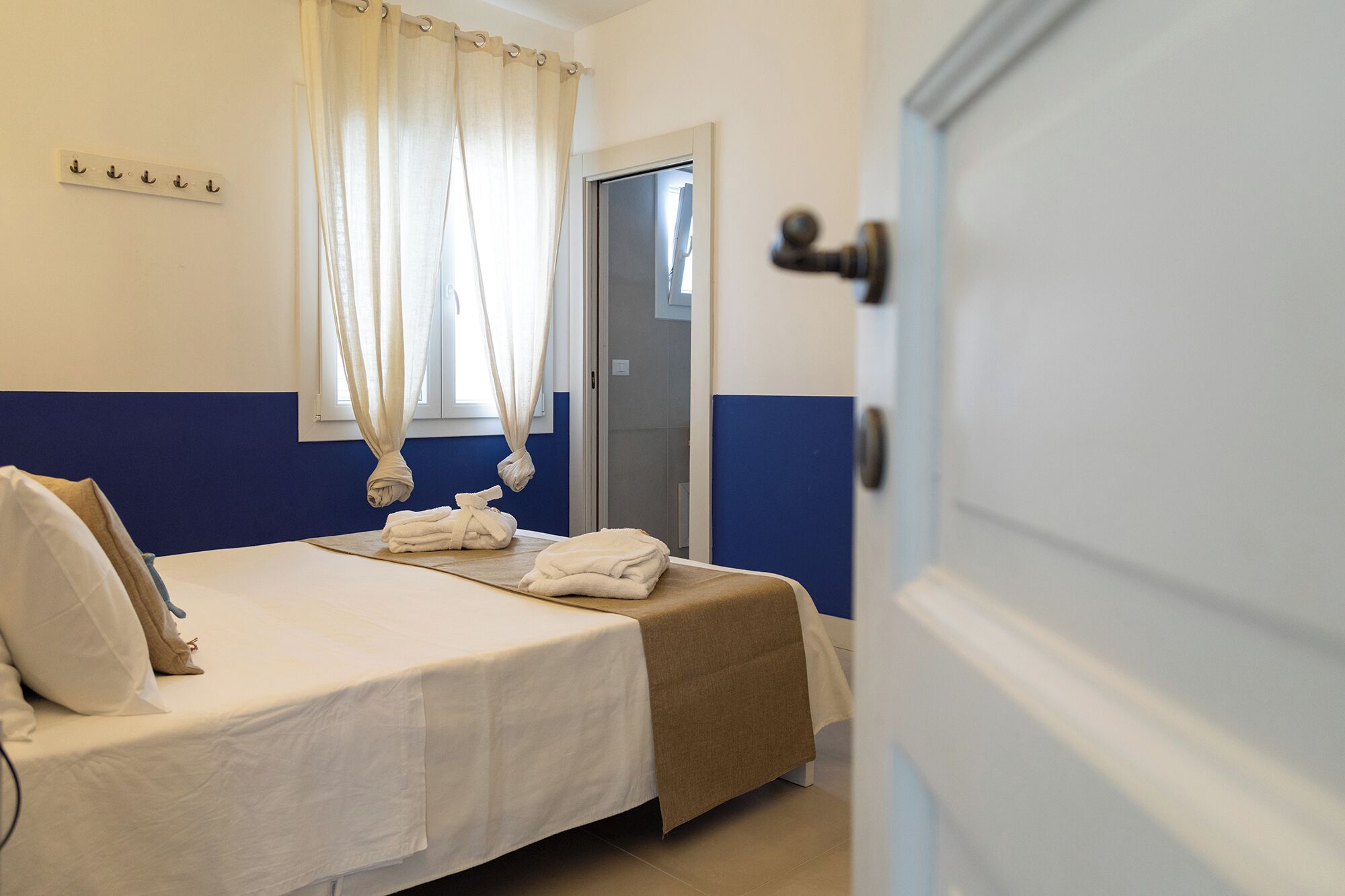 A hotel room with a bed, a bathroom door, and a coat rack with towels.