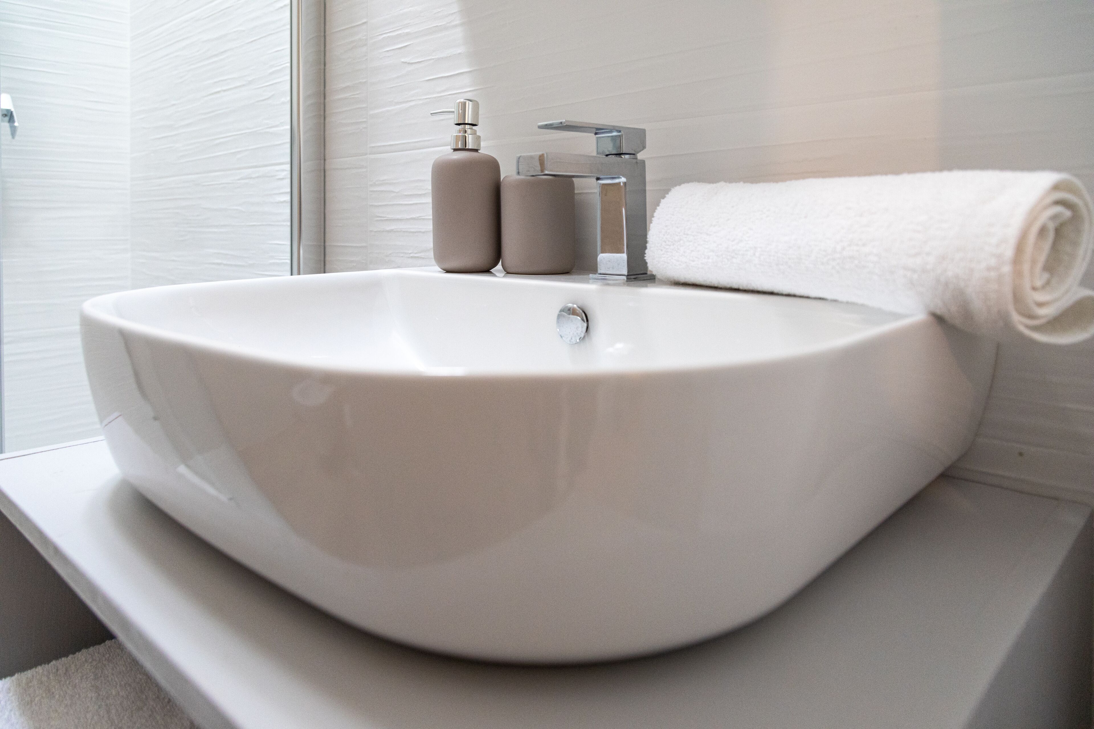Ein Badezimmer mit einem großen weißen Waschbecken, einem silbernen Wasserhahn und zwei beigen Flaschen auf der Ablagefläche.