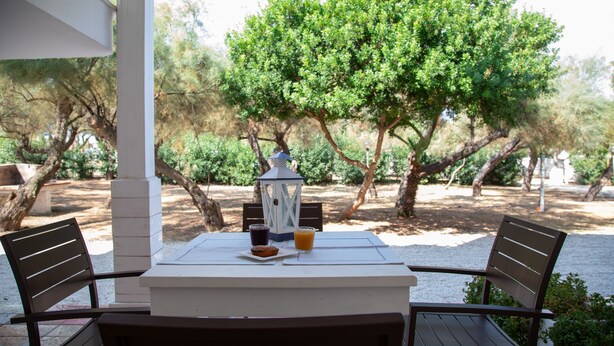 An outdoor dining area with a table and chairs, a lantern, and a view of trees and greenery.
