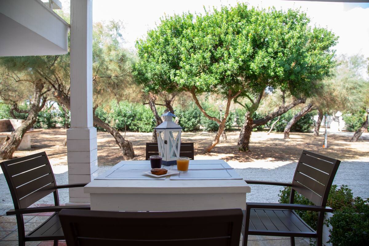 An outdoor dining area with a table and chairs, a lantern, and a view of trees and greenery.