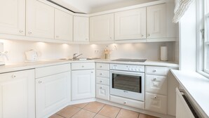 Una cocina moderna con armarios blancos, horno integrado y una ventana con cortinas blancas.
