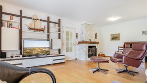 Un salon doté d’un téléviseur à écran plat, d’étagères en bois, d’une cheminée, de fauteuils en cuir et d’une bibliothèque.