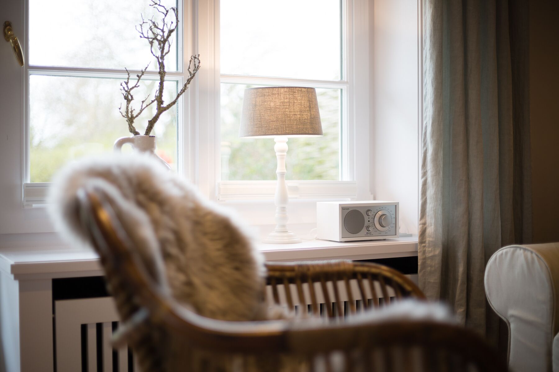 A chair with a fur throw, a lamp, and a radio on a windowsill.