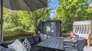 Ein Sitzbereich im Freien mit Tisch und Stühlen, umgeben von viel Grün.