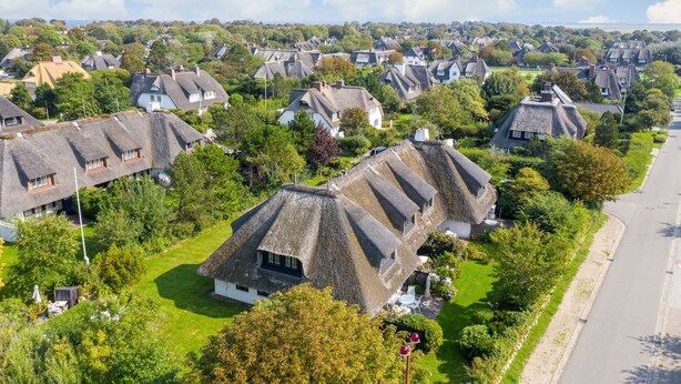 Een woonwijk met rieten daken, groene gazons en een heldere lucht.