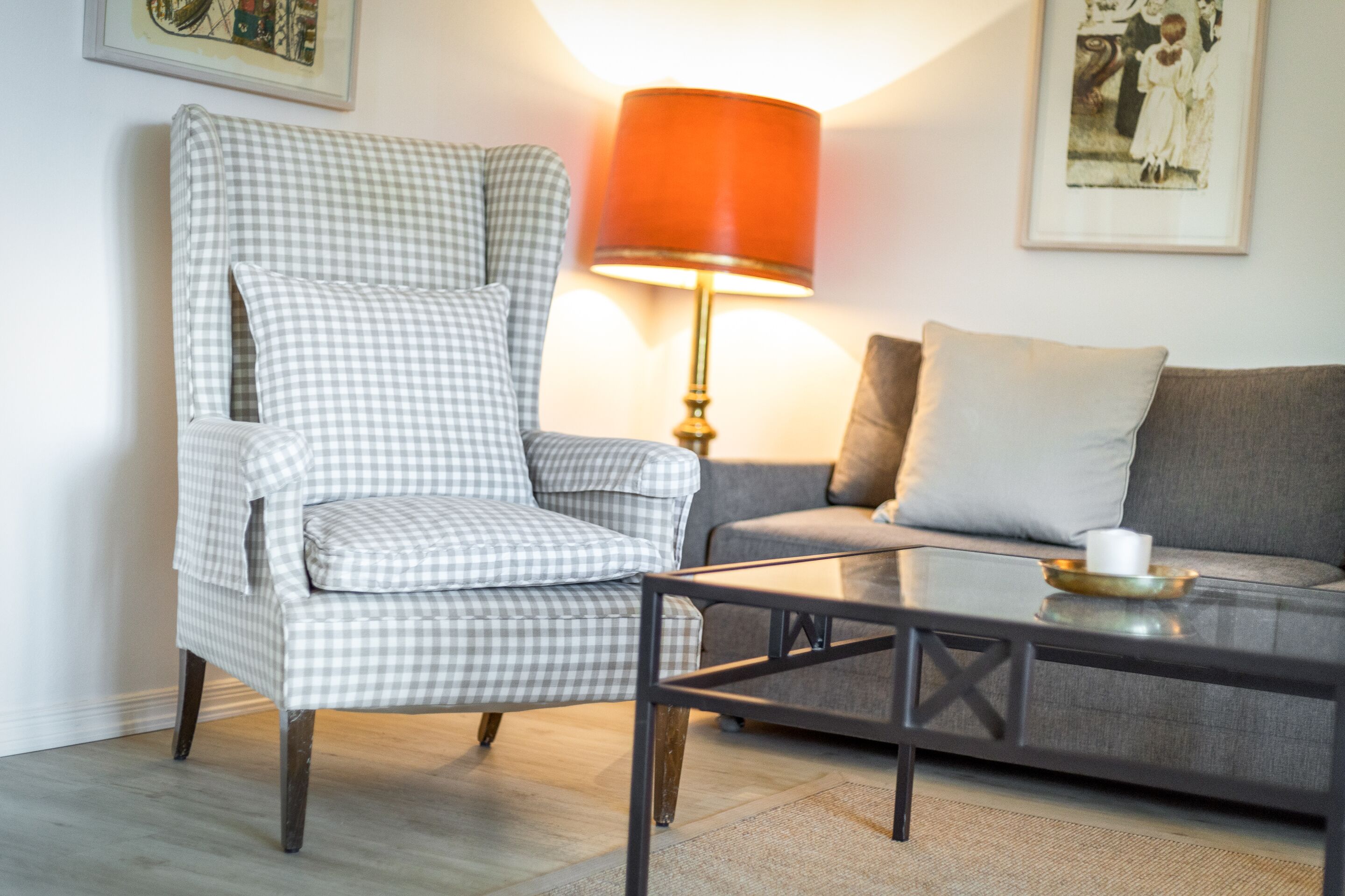 A checkered armchair, a grey sofa, a glass coffee table, and a red lamp.