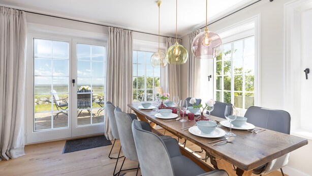 A dining area with a wooden table set for four, grey chairs, and a view through glass doors to an outdoor patio.