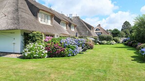 A row of thatched-roof cottages with white walls and multiple windows, surrounded by well-maintained gardens with various flowering plants. - Dieses Friesische Domizil Befindet Sich in Ruhiger Lage im Ortsteil Keitum (Sylt / OT Keitum)