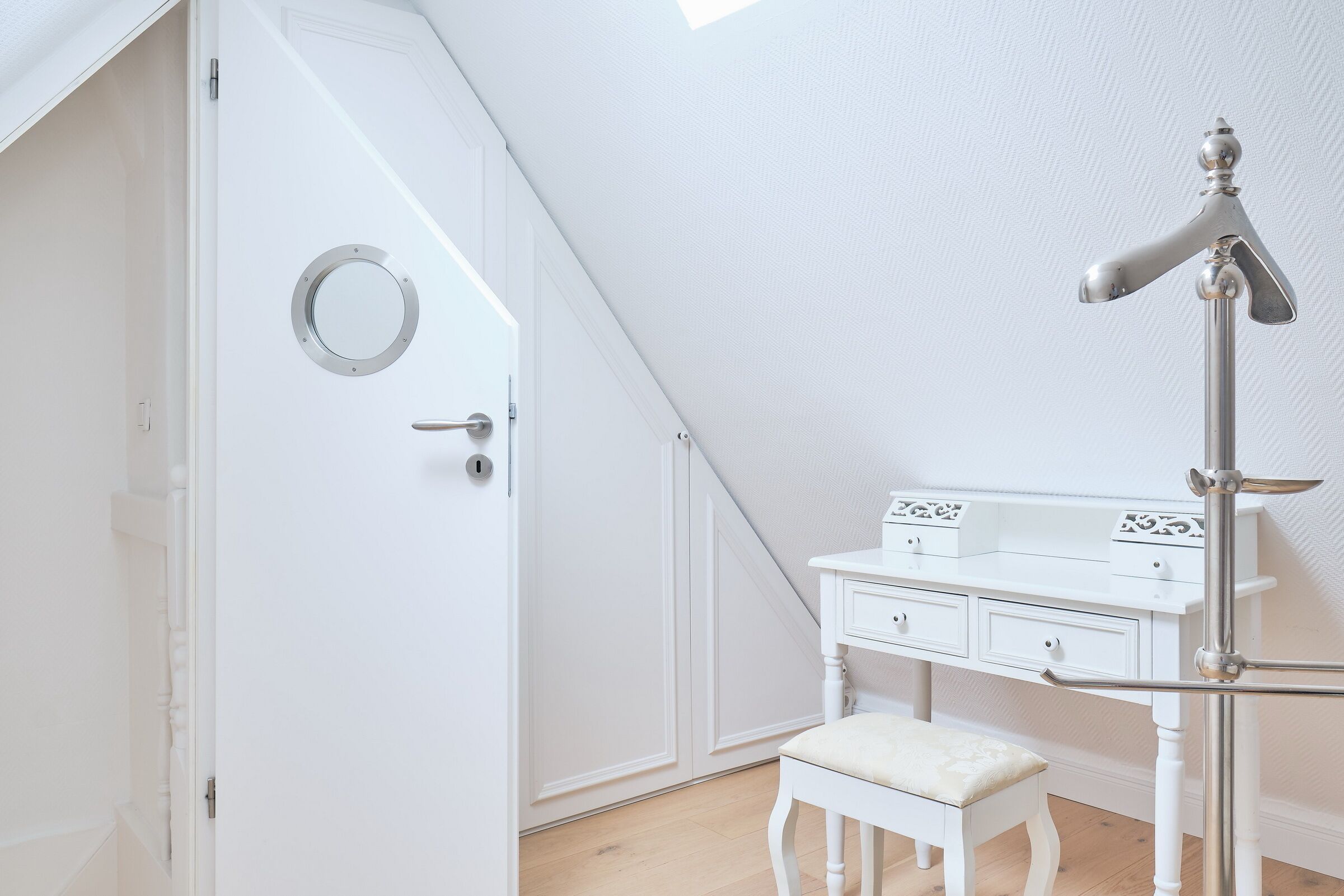A white room with a door, a vanity with drawers, and a stool.