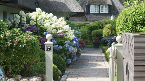 A pathway leading to a thatched-roof house with a well-maintained garden and a white mailbox with the number 7. - Dieses Friesische Domizil Befindet Sich in Ruhiger Lage im Ortsteil Keitum (Sylt / OT Keitum)
