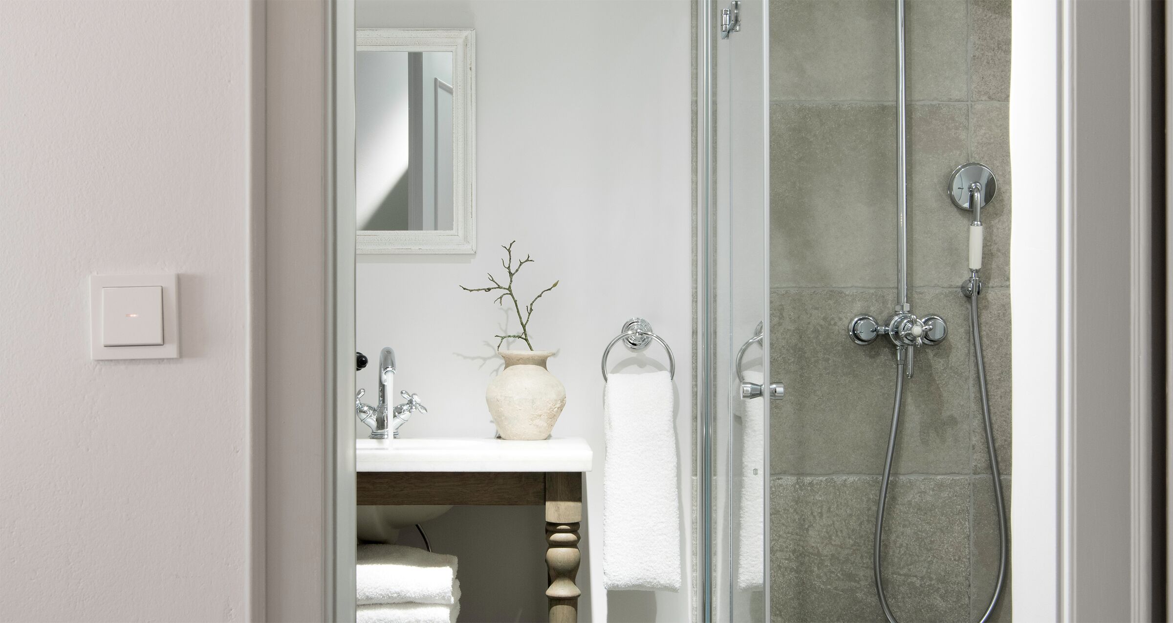 Un baño con ducha de vidrio, un lavamanos blanco con un florero y un espejo sobre el lavamanos.
