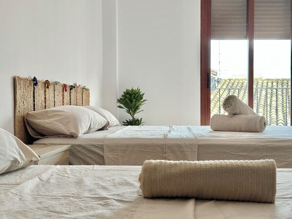 A hotel room with two beds, a small potted plant, and a view of a balcony.
