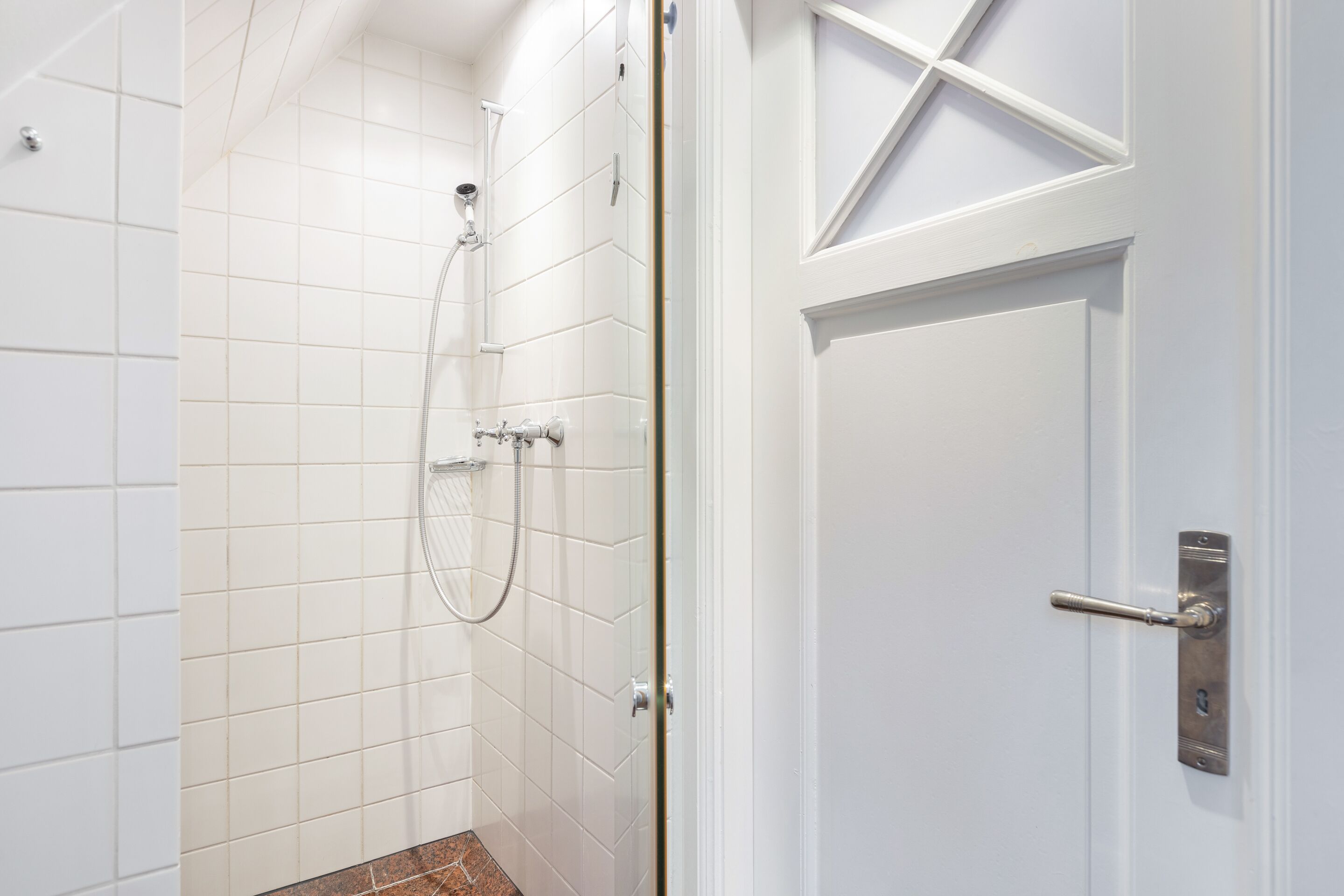 Ein Badezimmer mit weißen Fliesen, einer Duschkabine und einer Tür mit einem modernen Griff.