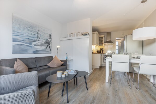 Una sala de estar moderna con un sofá gris, una mesa de centro y un comedor con sillas blancas y una mesa.