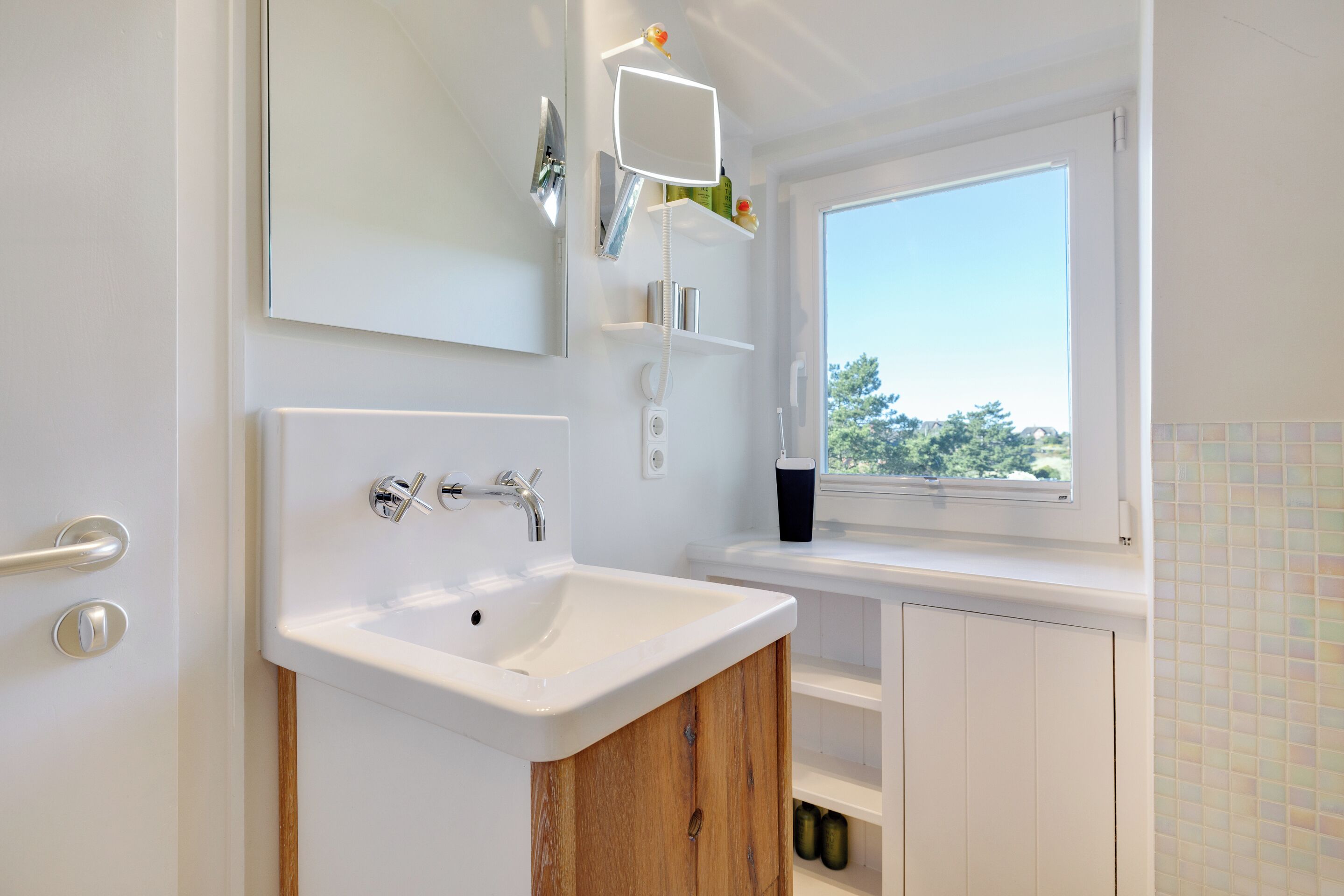 A modern bathroom with a white sink, a mirror, and a window.