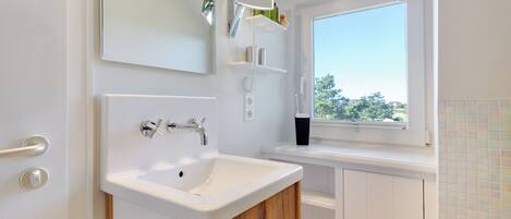 A modern bathroom with a white sink, a mirror, and a window.