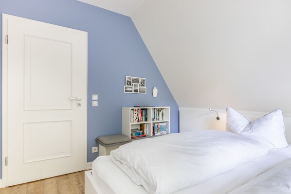 A bedroom with a white bed, a bookshelf, and a door. - Auszeit im Takerhof - Ferienwohnung in Wunderschöner Südlage in Keitum (Sylt / OT Keitum)