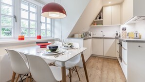 Moderni keittiö, jossa on valkoiset kaapit, ruokapöytä tuoleineen ja suuri ikkuna, josta tulee runsaasti luonnonvaloa.