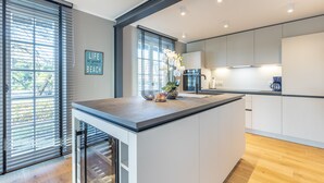 A modern kitchen with a central island, large windows with blinds, and a 'Life is good. Beach' sign. - Stina - Hoch Moderne Frisch Renovierte Oase, Bietet Großzügig Platz! (Sylt / OT Keitum)