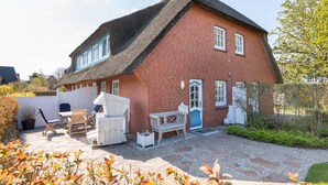 Una casa in mattoni rossi con tetto di paglia, un patio in pietra e mobili da esterno.