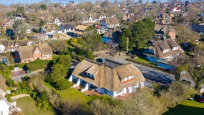 A village with thatched-roof houses, a main road, and a body of water in the background. - 2-raum Appartement Unter Reet im Herzen von Keitum (Sylt / OT Keitum)