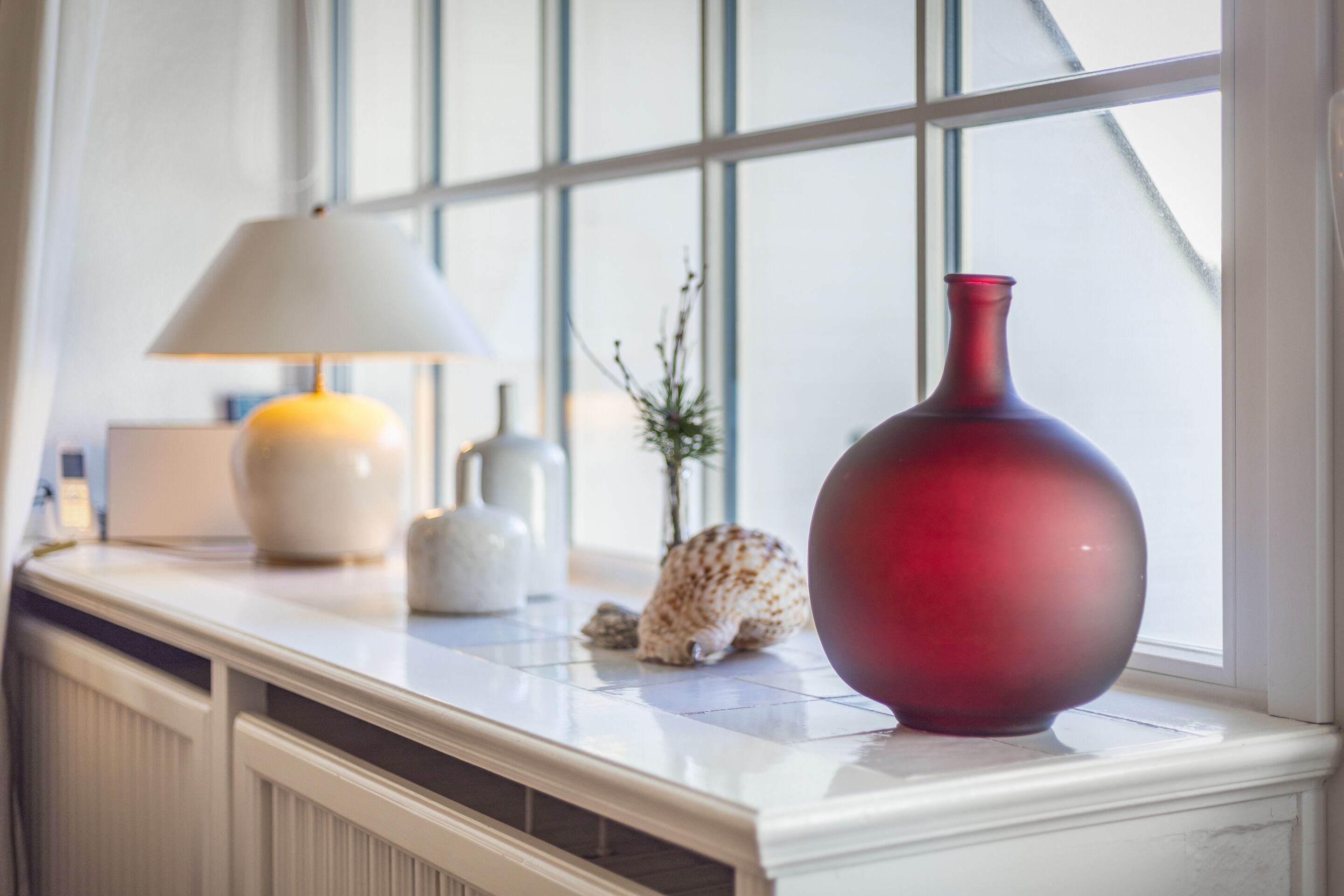 Een marmeren aanrecht met een rode vaas, een witte lamp en een decoratieve schelp.