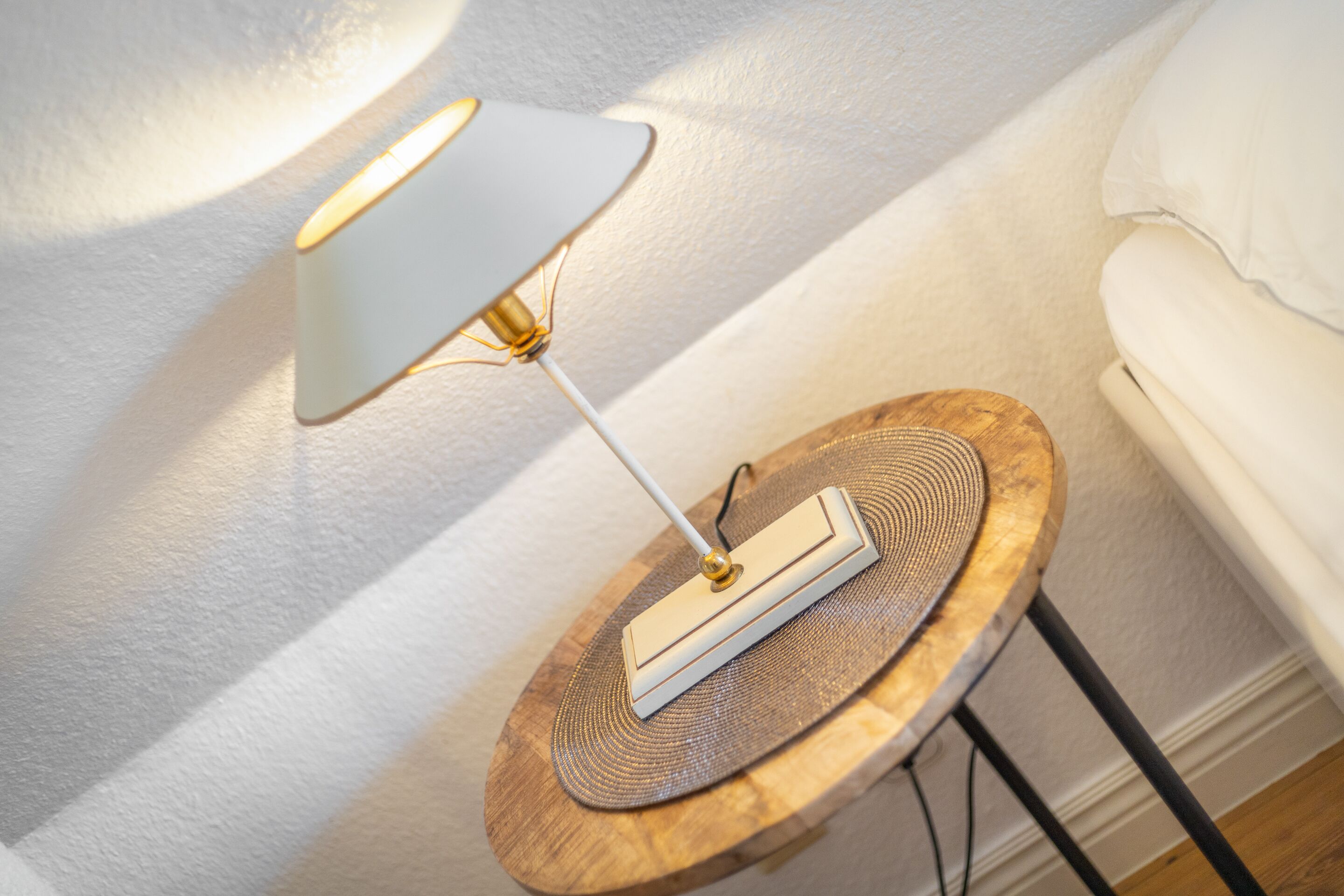Een moderne lamp op een houten bijzettafeltje naast een witte bank.