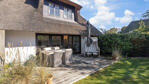 Une maison avec un toit de chaume, un espace extérieur aménagé et couvert, et une pelouse bien entretenue.
