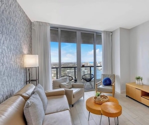 A modern living room with a sofa, armchairs, a coffee table, and a view of the city through large windows.