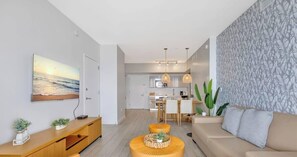 A modern living room with a sofa, a coffee table, a TV, and a dining area with a table and chairs.