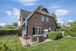 Traditional brick house with a thatched roof, featuring a patio area with outdoor furniture and a well-maintained lawn.