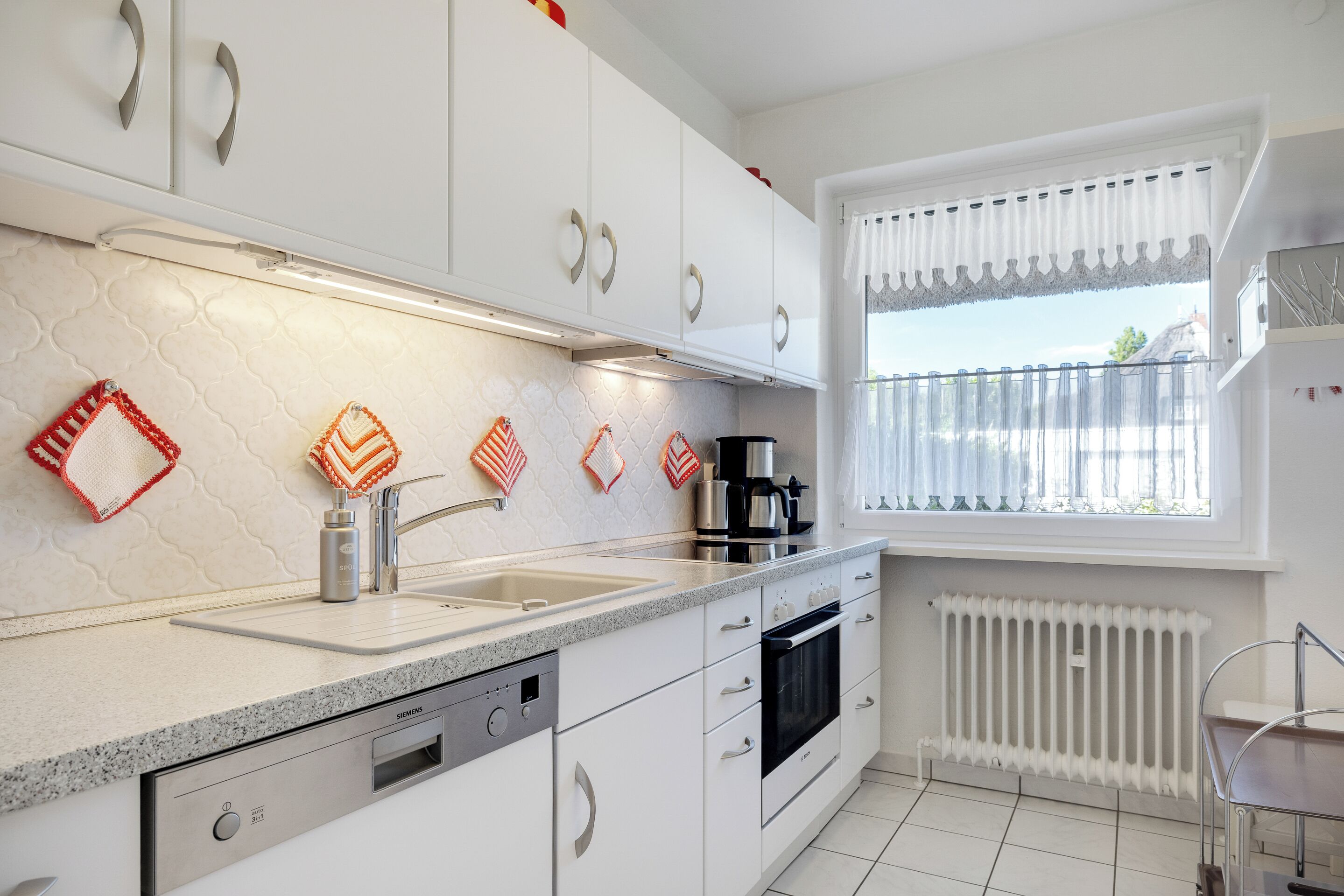 A modern kitchen with white cabinets, stainless steel appliances, and a window with a view.