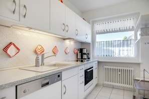 A modern kitchen with white cabinets, stainless steel appliances, and a window with a view.
