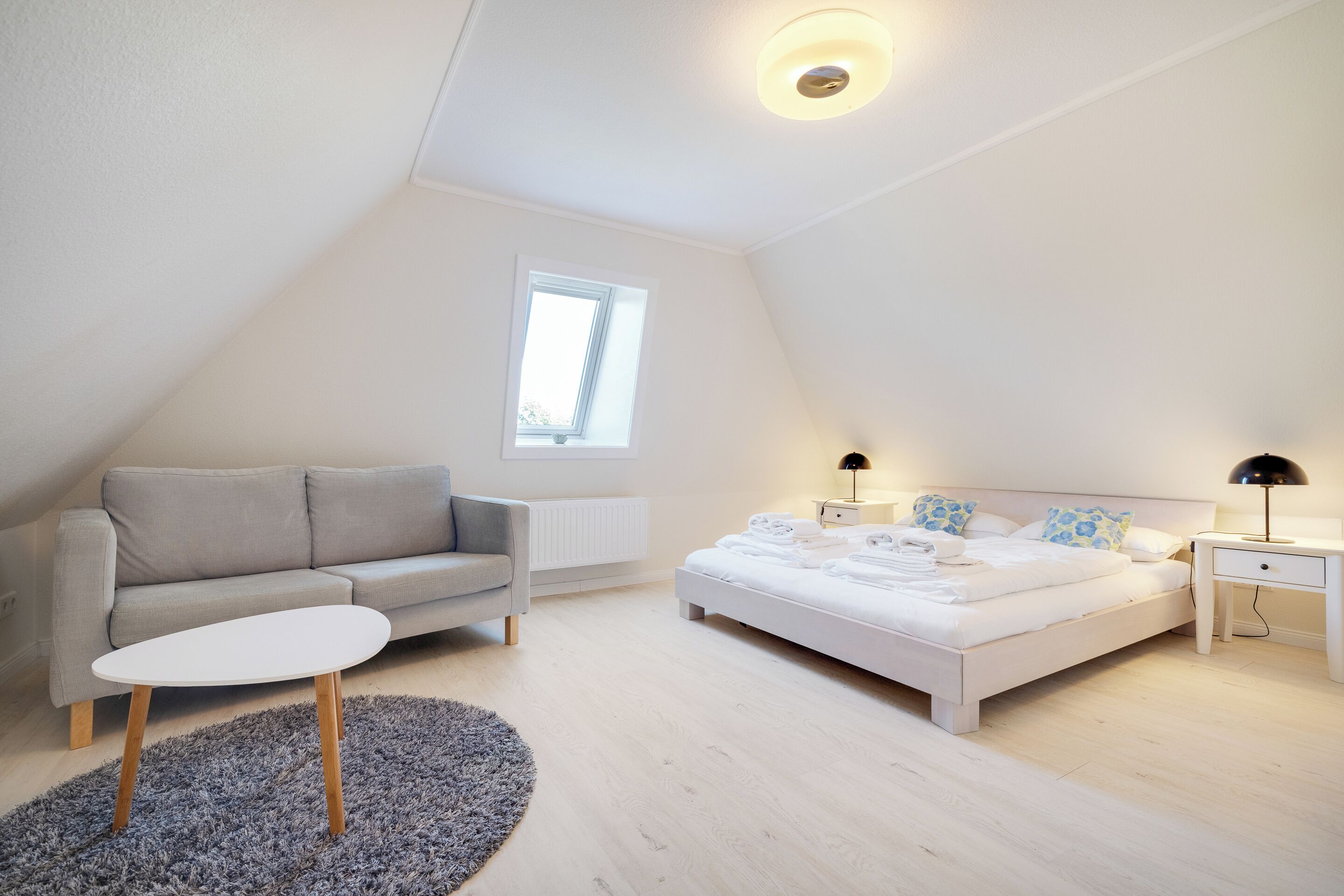 Un dormitorio con cama, sofá, una mesita, una lámpara y una ventana.