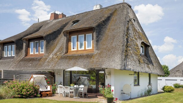 Een huis met rieten dak, een terras met tuinmeubilair en een schotelantenne.