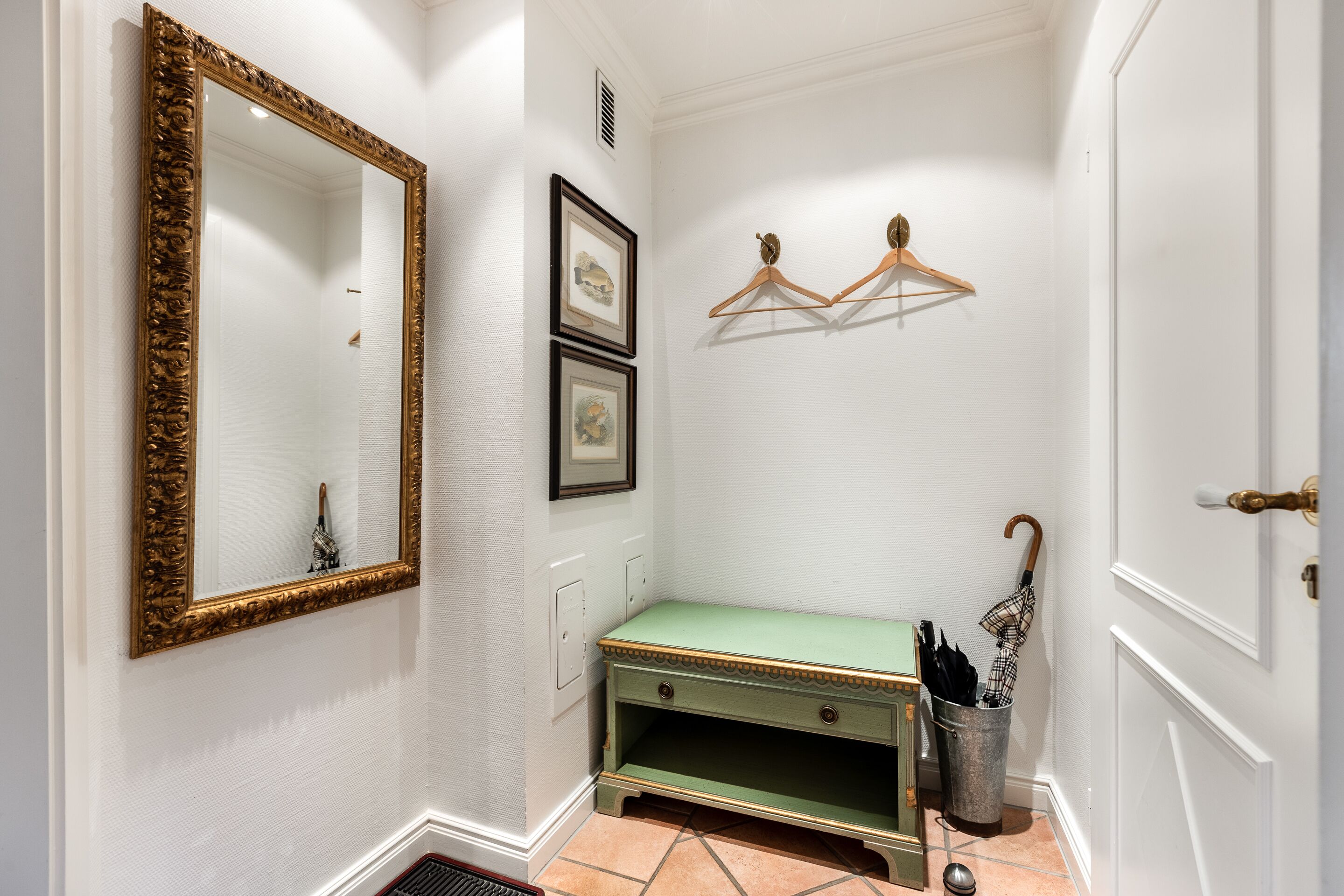 A hallway with a green bench, a gold-framed mirror, and wooden hangers on the wall.