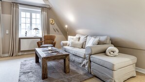 A cozy living room with a sofa, a wooden coffee table, and a chair. - Galeriesuite - Exklusive Ferienwohnung Unter Reet (Sylt / OT Archsum)