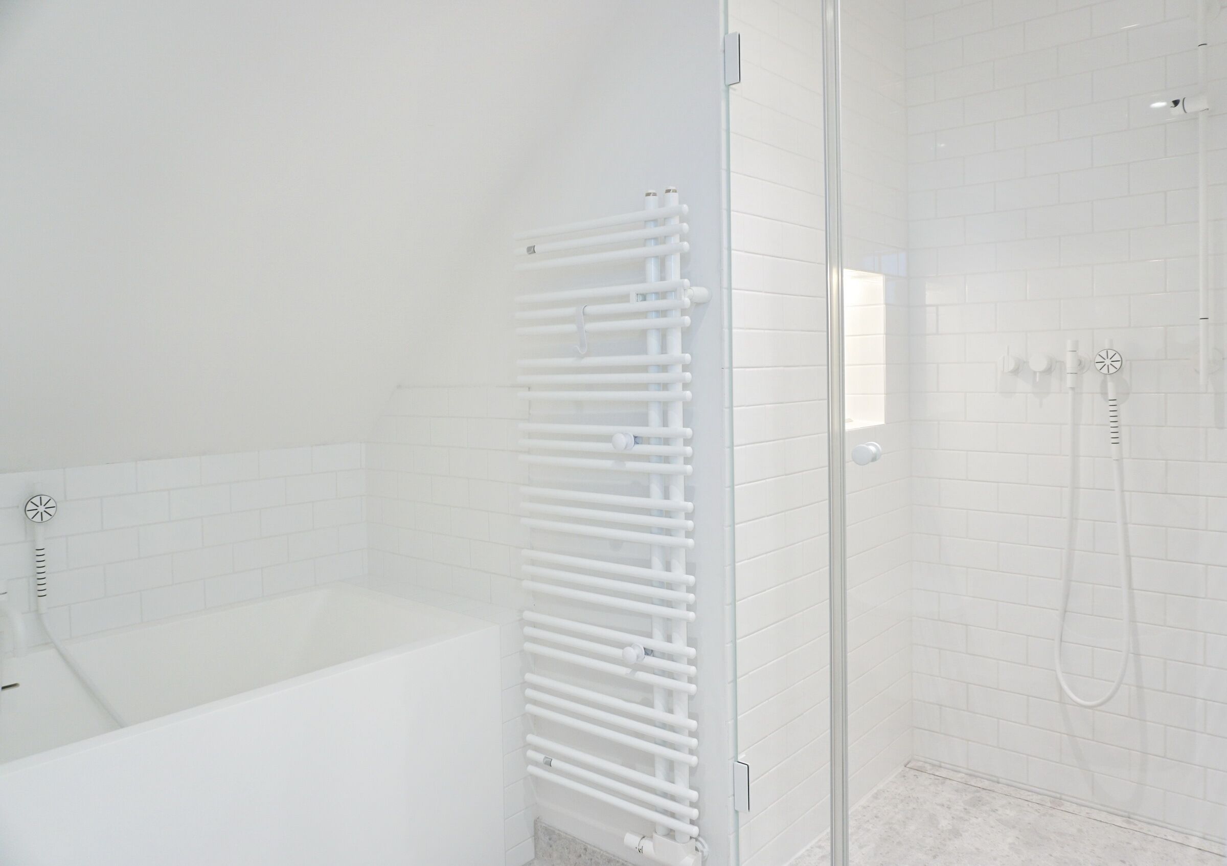 A modern bathroom with a glass shower enclosure, a white bathtub, and a built-in towel rack.