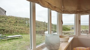 Habitación con ventanas amplias que dan a una zona verde y una vista lejana del mar.