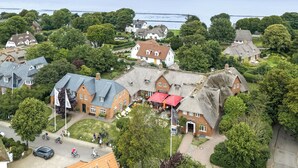 A coastal village with traditional architecture, a central building with a red roof, and a view of the sea.