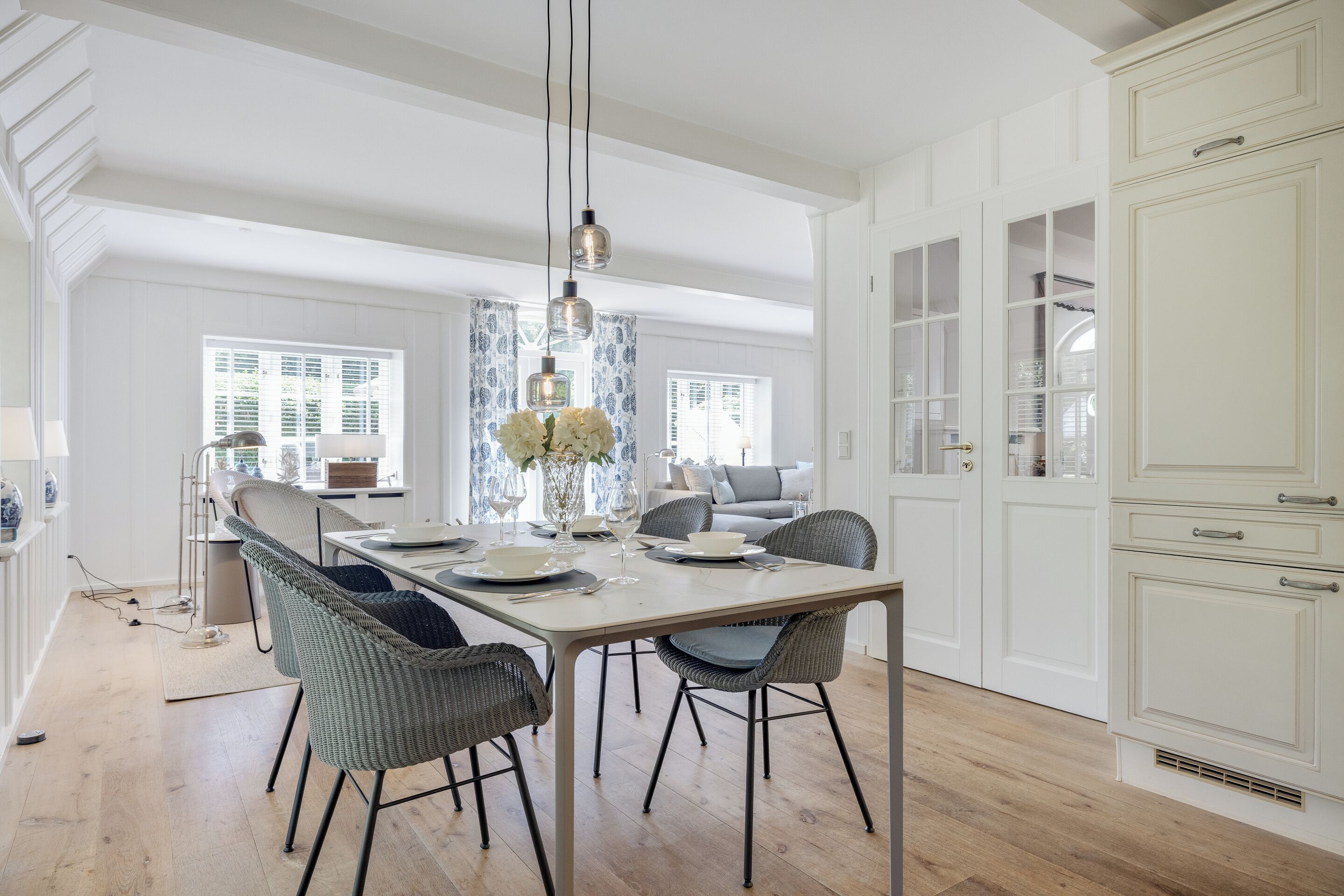 Un espace repas avec une longue table, des chaises en osier et un lustre.