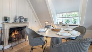 A dining area with a fireplace, wicker chairs, and a table set for a meal.