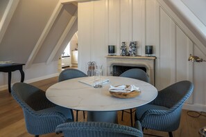 Un coin repas avec une table ronde, quatre chaises, une cheminée et une cuisine en arrière-plan.